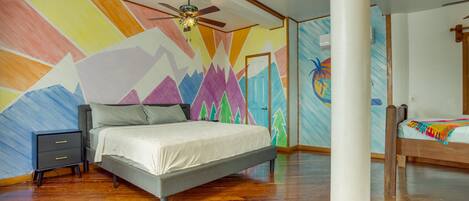 A bedroom with a bed, a nightstand, a ceiling fan, and a colorful wall mural.