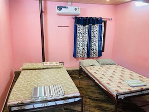 A room with two single beds, a window with blue curtains, an air conditioning unit, and a wall-mounted shelf.