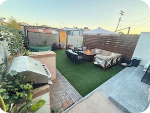 A backyard with artificial grass, a barbecue grill, outdoor furniture, and a wooden fence.