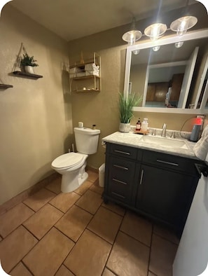 A bathroom with a toilet, sink, vanity, and a mirror with lights.