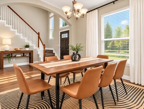 A dining area with a wooden table, six chairs, a chandelier, and a view of the outdoors through large windows. - Big Groups, Game Room, BBQ, Pet Friendly, Pool (Frisco)