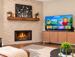 A modern living room with a fireplace, a flat-screen TV displaying PBS Kids, and a cozy seating area. - Big Groups, Game Room, BBQ, Pet Friendly, Pool (Frisco)