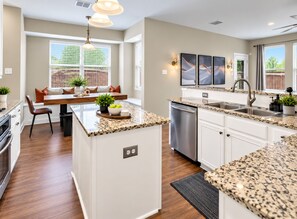 A modern kitchen with granite countertops, a built-in dishwasher, and a dining area with a bench and potted plants. - Big Groups, Game Room, BBQ, Pet Friendly, Pool (Frisco)