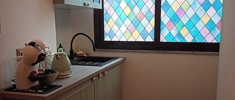A kitchen with a window, a kettle, a coffee maker, and a sink.