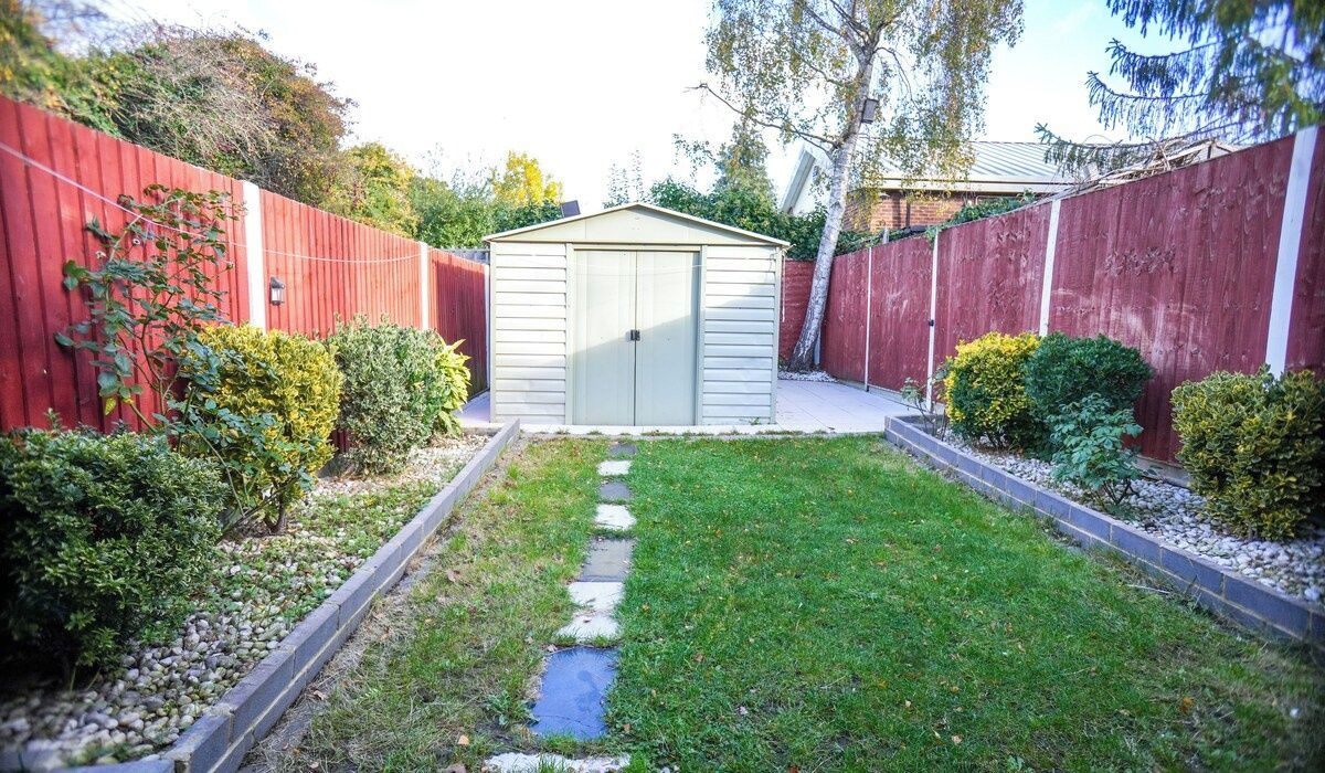 A backyard with a shed, a stone pathway, and various shrubs.