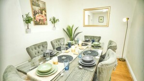 Ein Esszimmer mit einem Tisch, gedeckten Tellern, Gläsern und Kerzen, umgeben von Polsterstühlen.