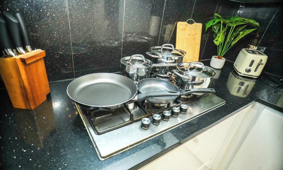 Una cocina con estufa, ollas, sartenes, un tostador y una planta.
