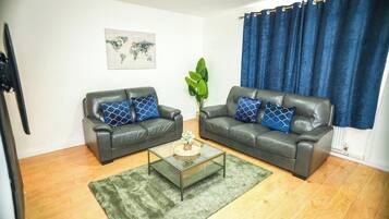 A living room with two leather sofas, a glass coffee table, a green rug, a world map artwork, and blue curtains.