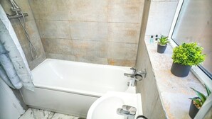 Ein Badezimmer mit einer Badewanne, einem Waschbecken und einem Fenster mit Blumentöpfen.