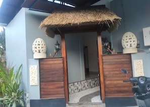 Une entrée de maison avec un avant-toit en chaume, des portes en bois, des sphères décoratives et un scooter garé à l’extérieur.