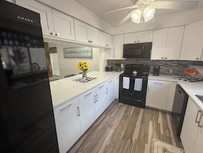 A modern kitchen with white cabinetry, a black refrigerator, and a microwave. - Cozy 2-bedroom condo in peaceful Port Richey with AC (Port Richey)
