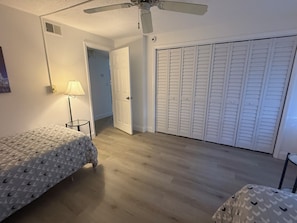 A bedroom with two beds, a ceiling fan, a lamp, and a closet with louvered doors. - Cozy 2-bedroom condo in peaceful Port Richey with AC (Port Richey)