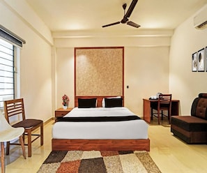 A hotel room with a bed, a desk, a chair, a sofa, a ceiling fan, and a window with blinds. - Classic Goldens Residency (Puducherry)