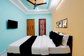 A bedroom with a bed, a ceiling fan, a TV, and a door with a decorative panel.