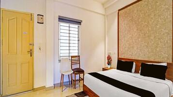 A hotel room with a bed, a chair, a window with blinds, and a door.