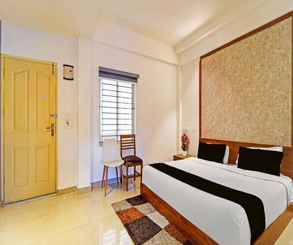 A hotel room with a bed, a chair, a window with blinds, and a door. - Classic Goldens Residency (Puducherry)
