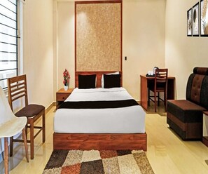 A hotel room with a bed, a desk, a chair, a sofa, and a window with blinds. - Classic Goldens Residency (Puducherry)