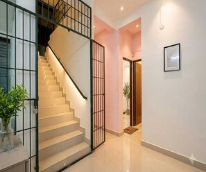 A staircase with a metal railing leading to a landing, a door with a mat, and a framed picture on the wall. - Classic Goldens Residency (Puducherry)