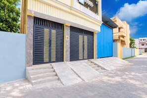 A residential building with a gated entrance, a staircase leading to the entrance, and a blue garage door.
