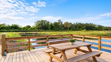 A wooden deck with picnic tables and benches overlooking a pond and forest.