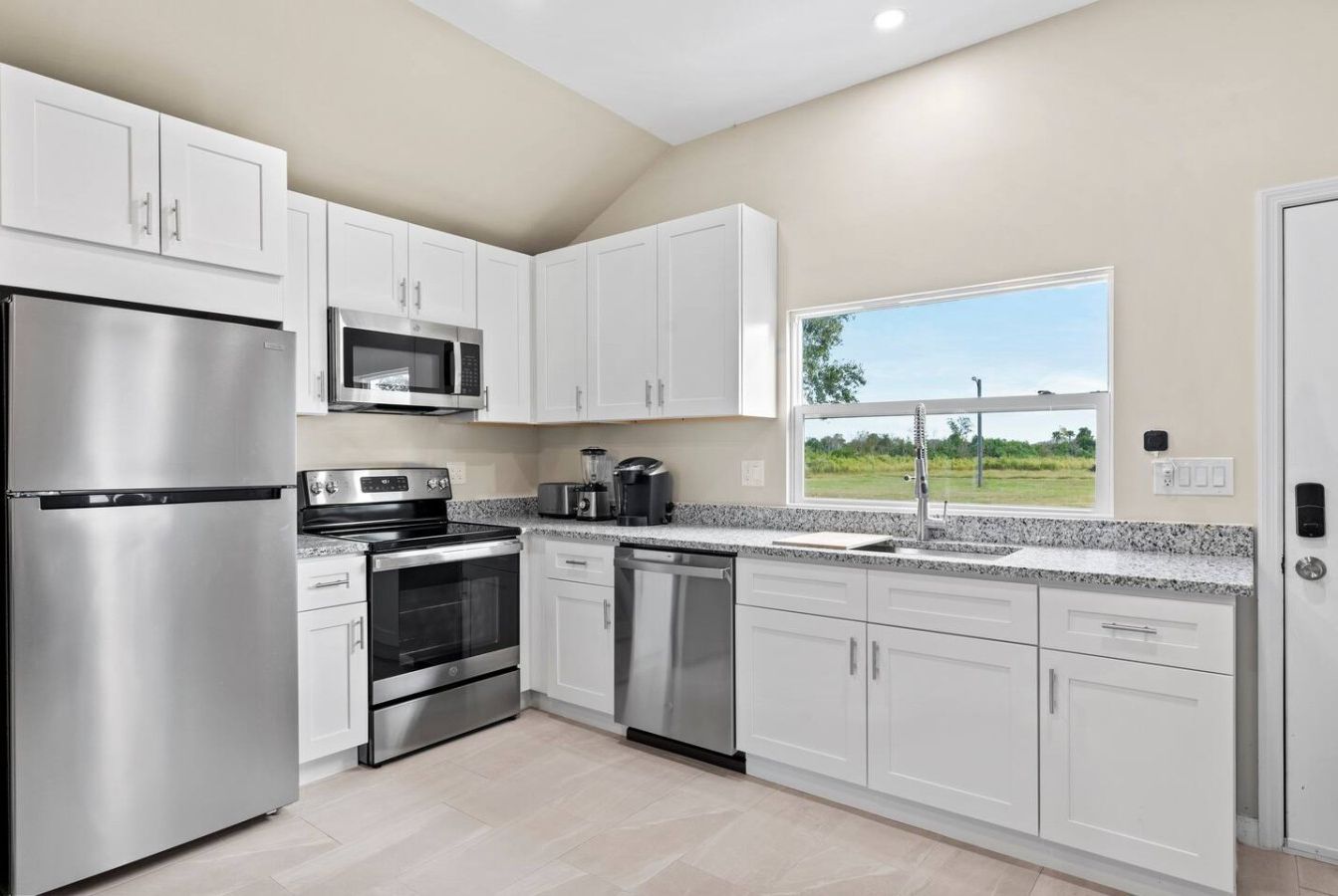 A modern kitchen with stainless steel appliances, white cabinetry, and a view of the outdoors.
