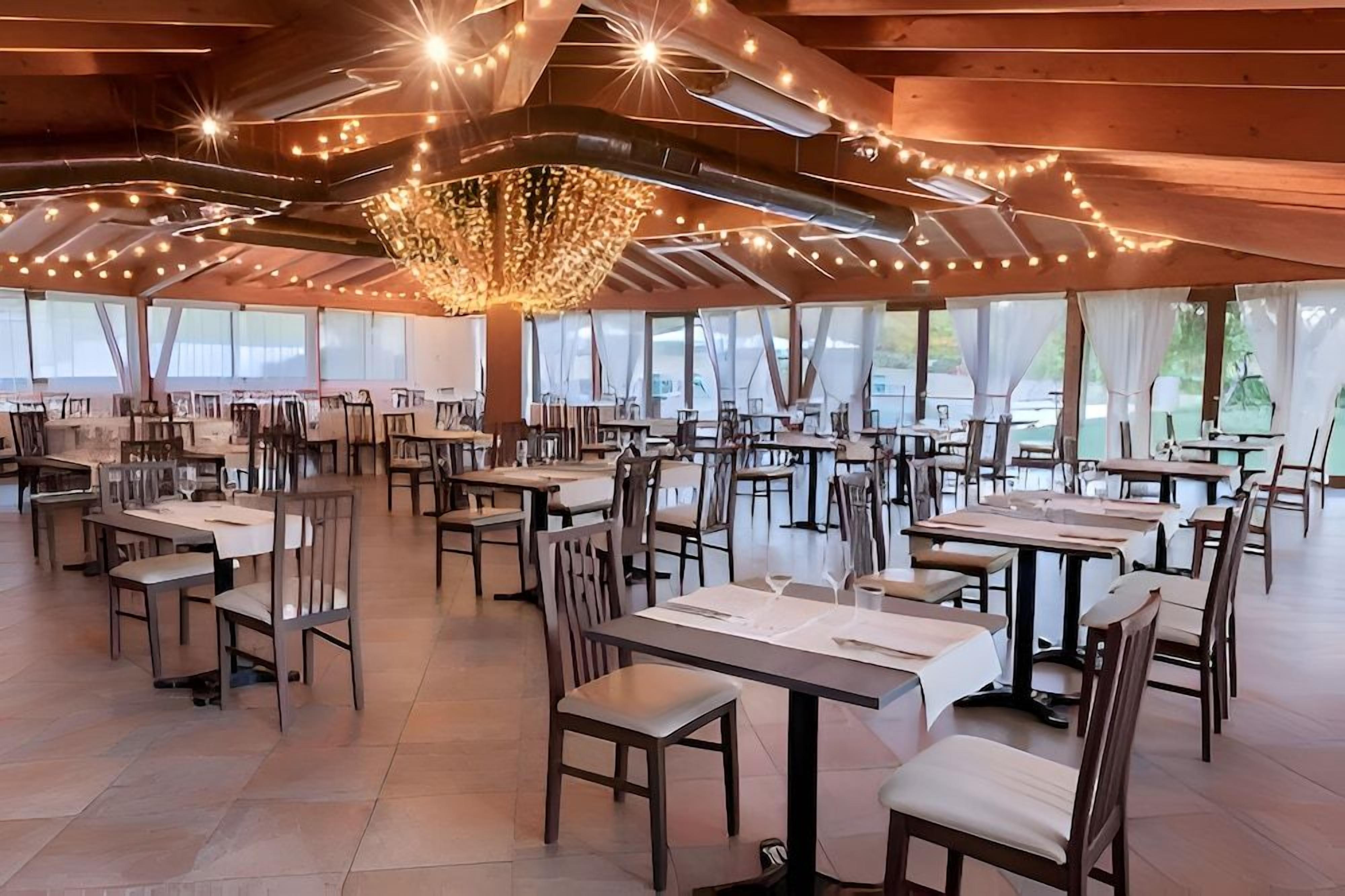 Un'ampia sala da pranzo con diversi tavoli e sedie, grandi finestre e un lampadario decorativo.
