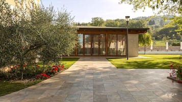 Un sentiero conduce a un edificio con facciata in vetro, immerso nel verde e sotto un cielo sereno.
