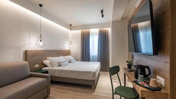 Una moderna camera d'hotel con un letto, un divano, una scrivania con una macchina del caffè e un televisore montato a parete.