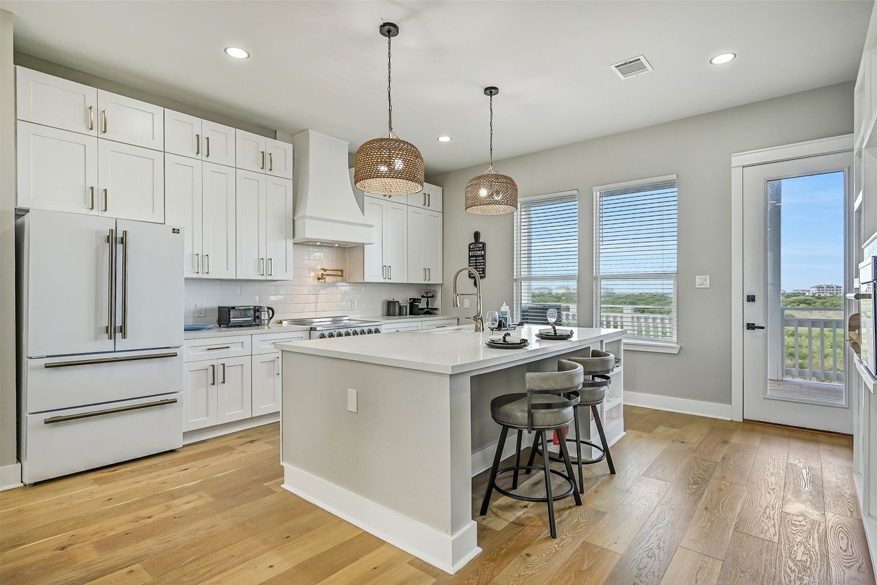 A modern kitchen with white cabinetry, a central island, pendant lighting, and a view through the window.