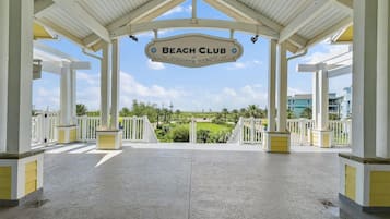 A covered outdoor area with a sign reading 'Beach Club at Pointe West,' featuring a view of a landscaped area and buildings in the background.