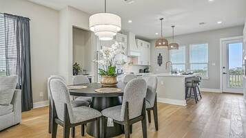 A modern kitchen with a central island, pendant lighting, and a dining area with a round table and chairs.