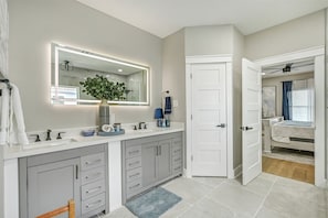 Un baño moderno con un espejo grande, un lavamanos y un inodoro. Hay un perchero y una planta en la encimera.