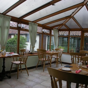 A conservatory with wooden-framed glass panels, hexagonal floor tiles, and a dining table set for four.