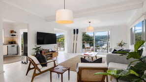 A modern living room with a flat-screen TV, comfortable seating, a dining area, and a view of the outdoors. - Sunny 3 bed cottage plus bunkhouse (HARDYS BAY)