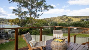 A deck with two wicker chairs and a round table, overlooking a lake and hills. - Sunny 3 bed cottage plus bunkhouse (HARDYS BAY)