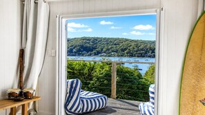 Ein Balkon mit Blick auf bewaldetes Gebiet und ein Gewässer mit Booten. Ein Holztisch mit Schlagzeug und einem Streifen-Kissen.