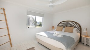 Ein Schlafzimmer mit Bett, Fenster, Deckenventilator, Nachttisch und Beistelltisch.