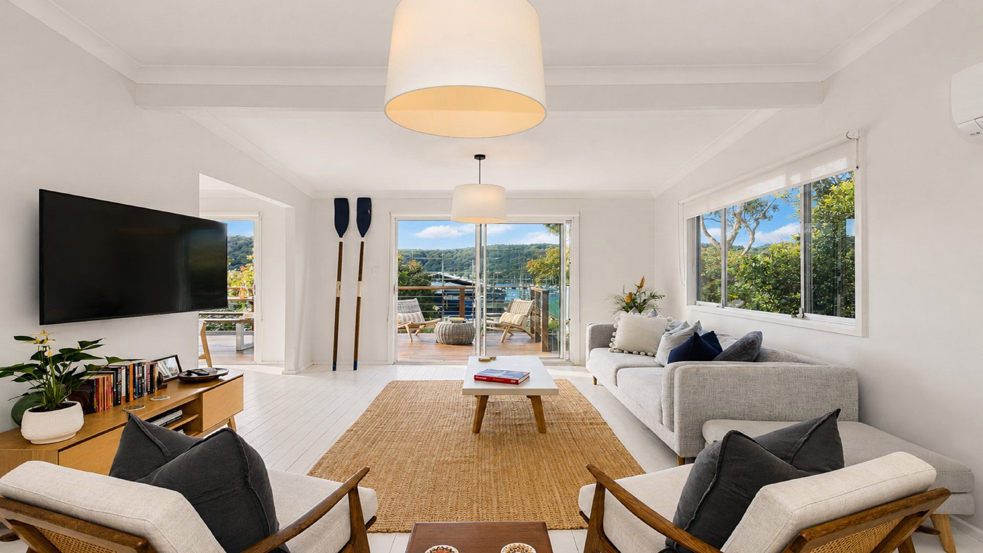 Ein modernes Wohnzimmer mit Fernseher, einer Couch, einem Couchtisch und Blick auf einen Balkon mit Gartenmöbeln.
