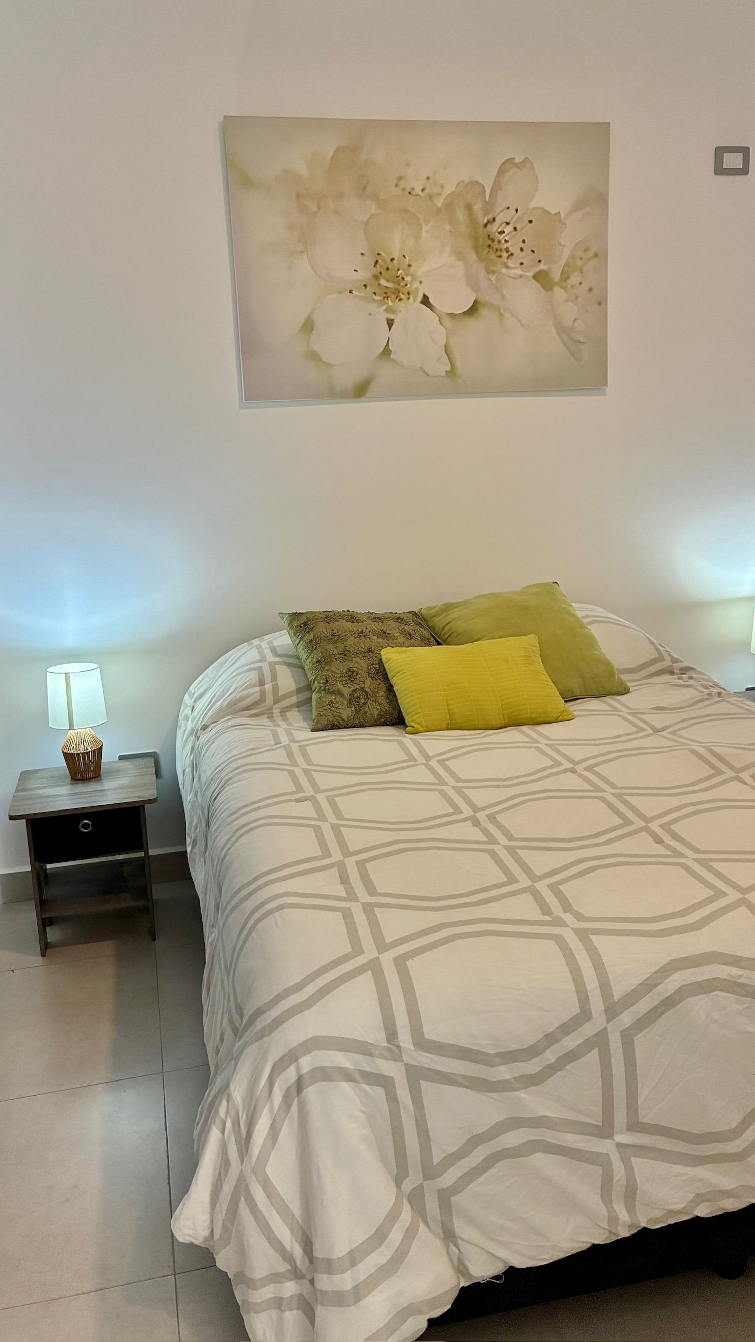 A bedroom with a bed, a nightstand, a lamp, and a wall-mounted painting.