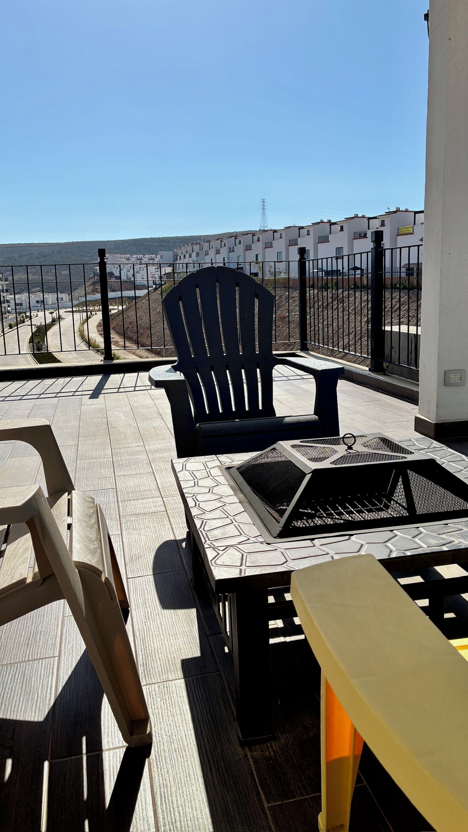 A balcony with a black chair, a yellow table, and a fire pit.