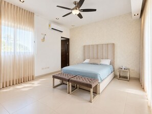 A modern bedroom with a bed, a bench, a ceiling fan, and an air conditioning unit. - Jounieh House | Unique, Spacious Home with Private Pool (Cozumel)
