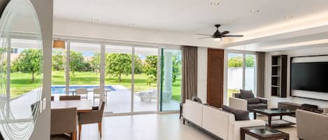 A modern living room with a flat-screen TV, comfortable seating, and a glass door leading to a pool area.