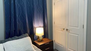 Ein Schlafzimmer mit einem Bett, einem Nachttisch mit Lampe, einer Tür und einem Vorhang mit Wellenmuster.
