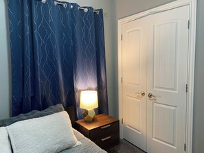 Ein Schlafzimmer mit einem Bett, einem Nachttisch mit Lampe, einer Tür und einem Vorhang mit Wellenmuster.