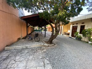 A covered outdoor area with a bicycle, a tree, and a building with a door and windows. - Hotel O Wisma Pramuka Syariah (West Cirebon)