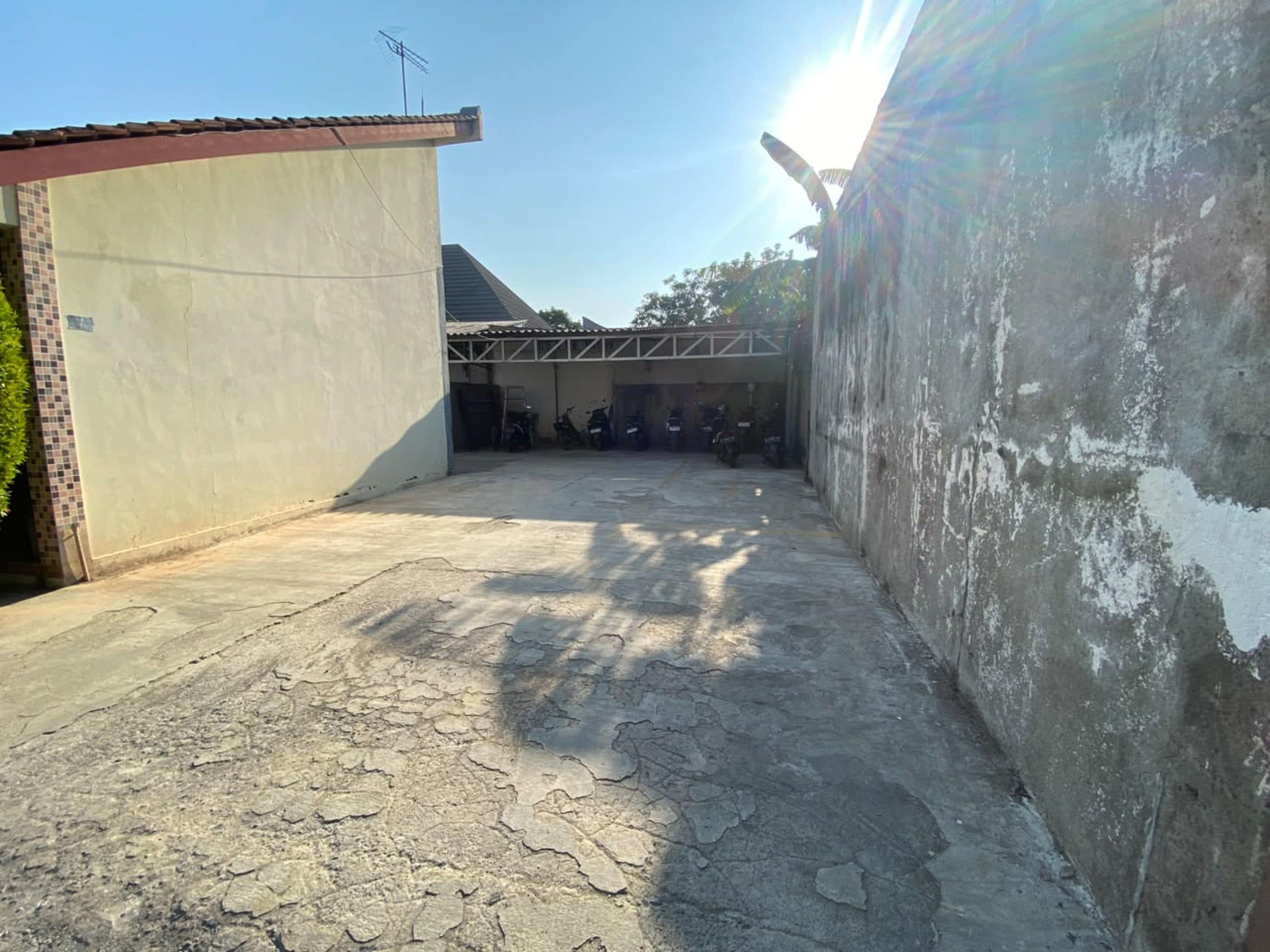 Une cour avec un sol en béton, un bâtiment doté d’un toit en tuiles et un mur dont la peinture s’écaillait.