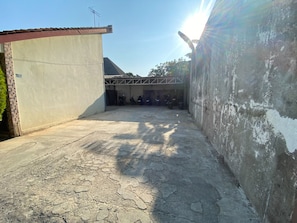 Un patio con piso de concreto, un edificio con techo de tejas y una pared con pintura descascarada.