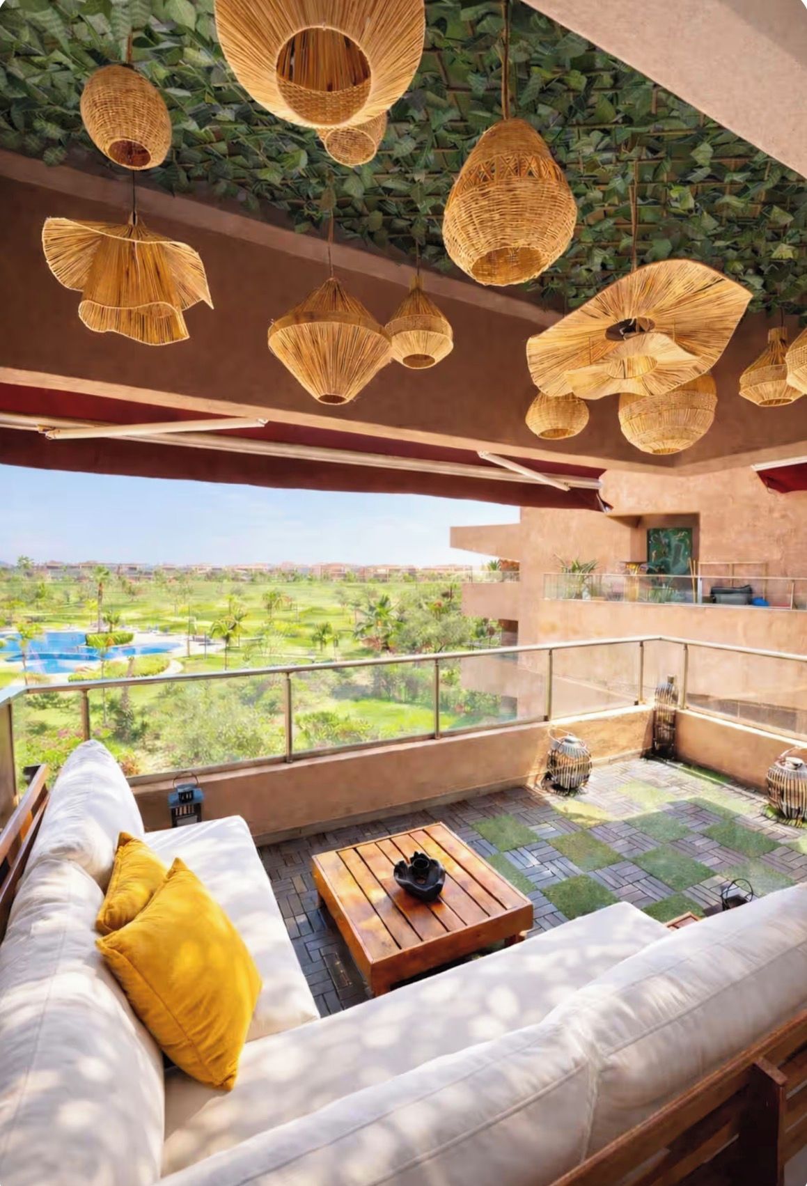 A balcony with a view of a green landscape, wicker hanging lamps, and a wooden table with a black object on it.