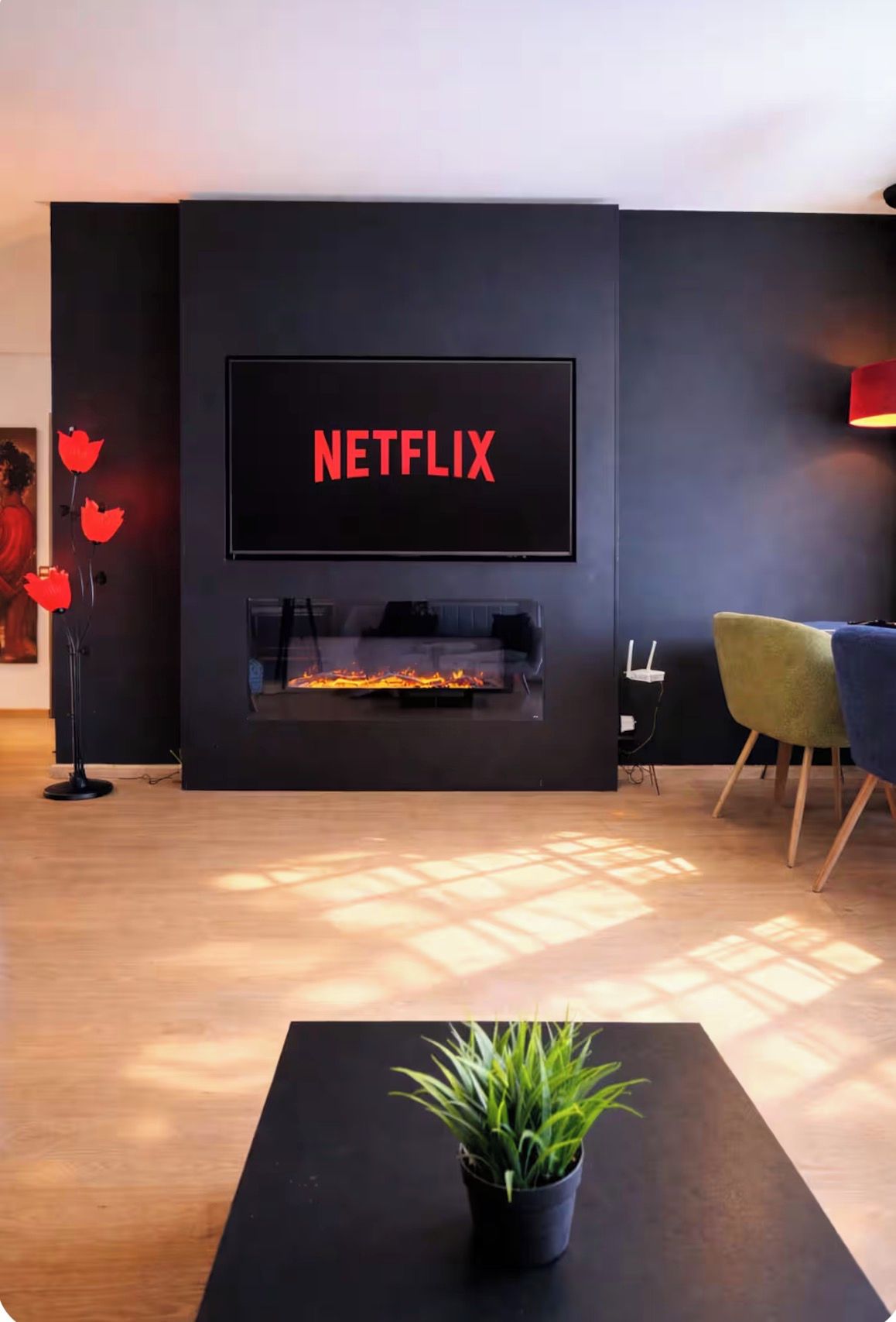 Una sala de estar moderna con chimenea, un televisor de pantalla plana montado en la pared y una planta en maceta sobre una mesa.