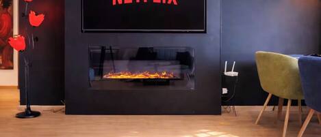 Una sala de estar moderna con chimenea, un televisor de pantalla plana montado en la pared y una planta en maceta sobre una mesa.